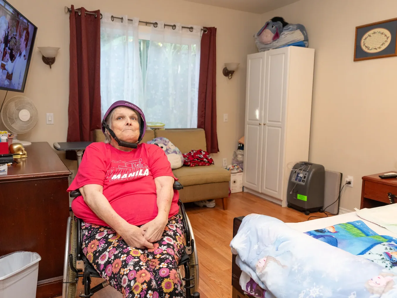 Resident in wheelchair wearing safety helmet seated in comfortable furnished living room of residential care facility